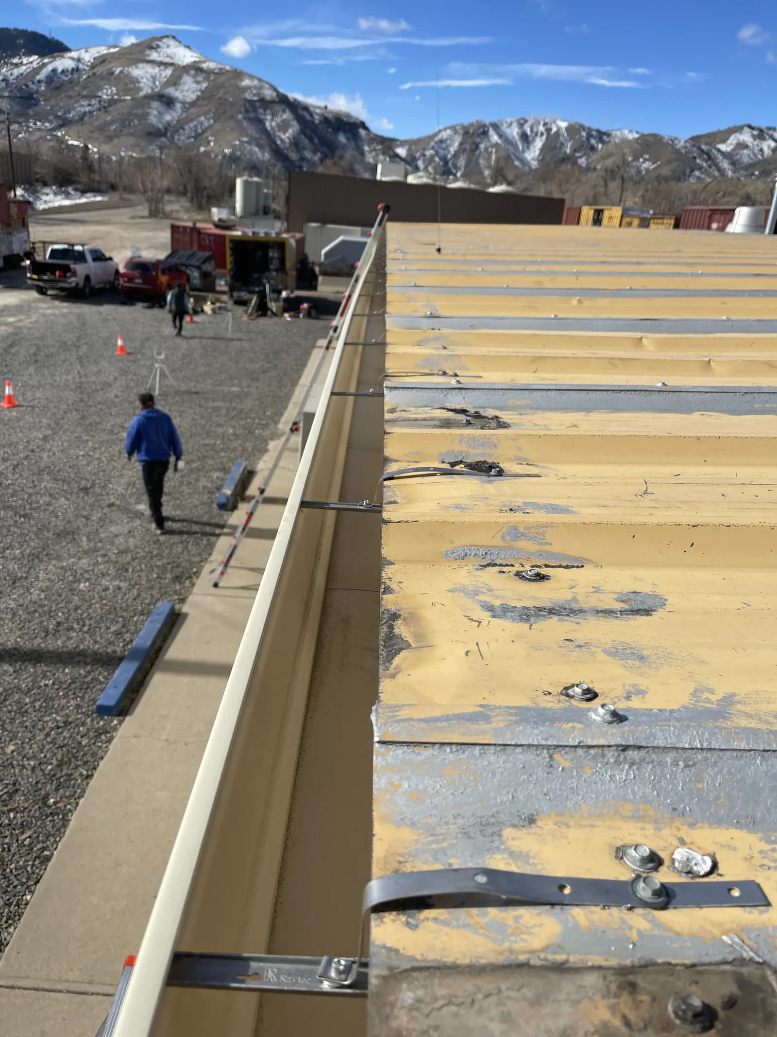 Worn yellow-coated metal panels with exposed fasteners alongside a long gutter