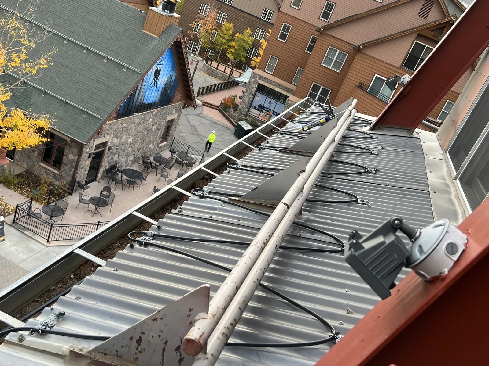 Gray metal roof panels, mounted rails and cables beside a gutter and adjoining wall