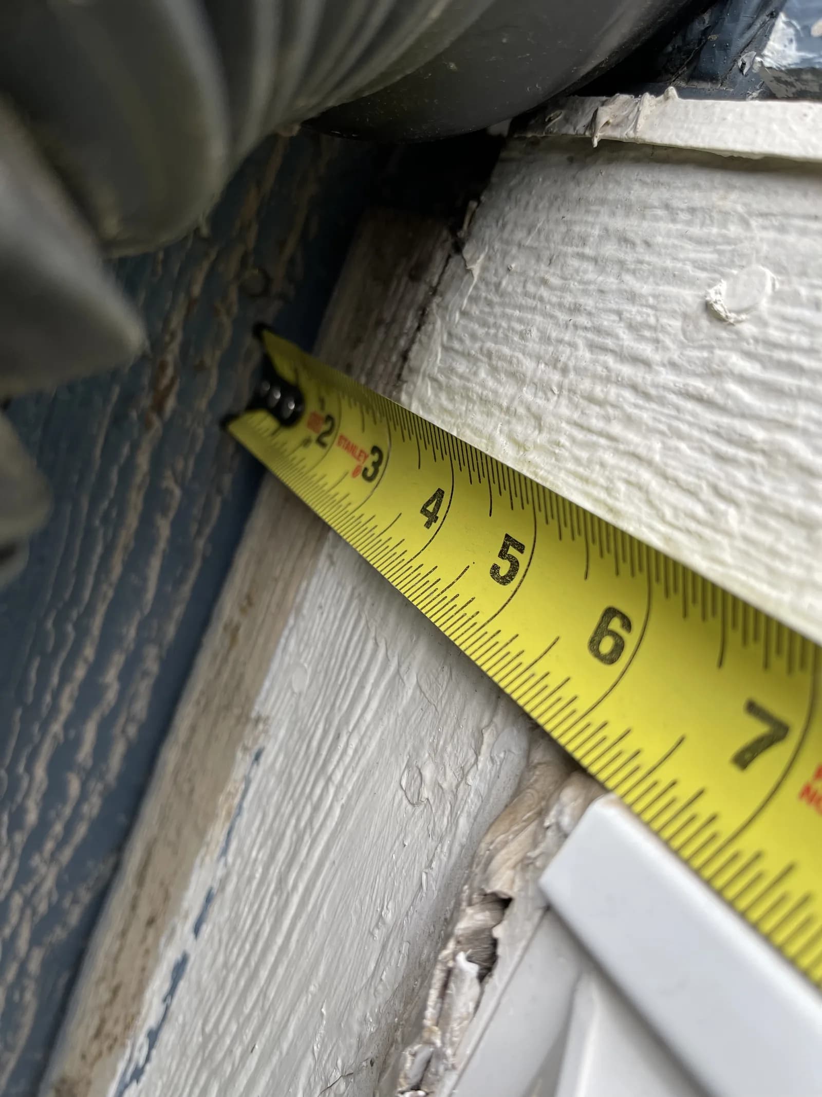A tape measure held at the junction of exterior trim and siding