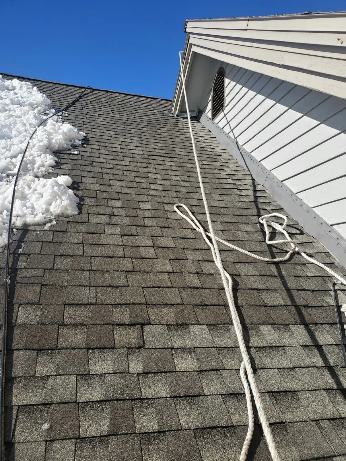 Shingle roof beside a wall with snow and rope visible