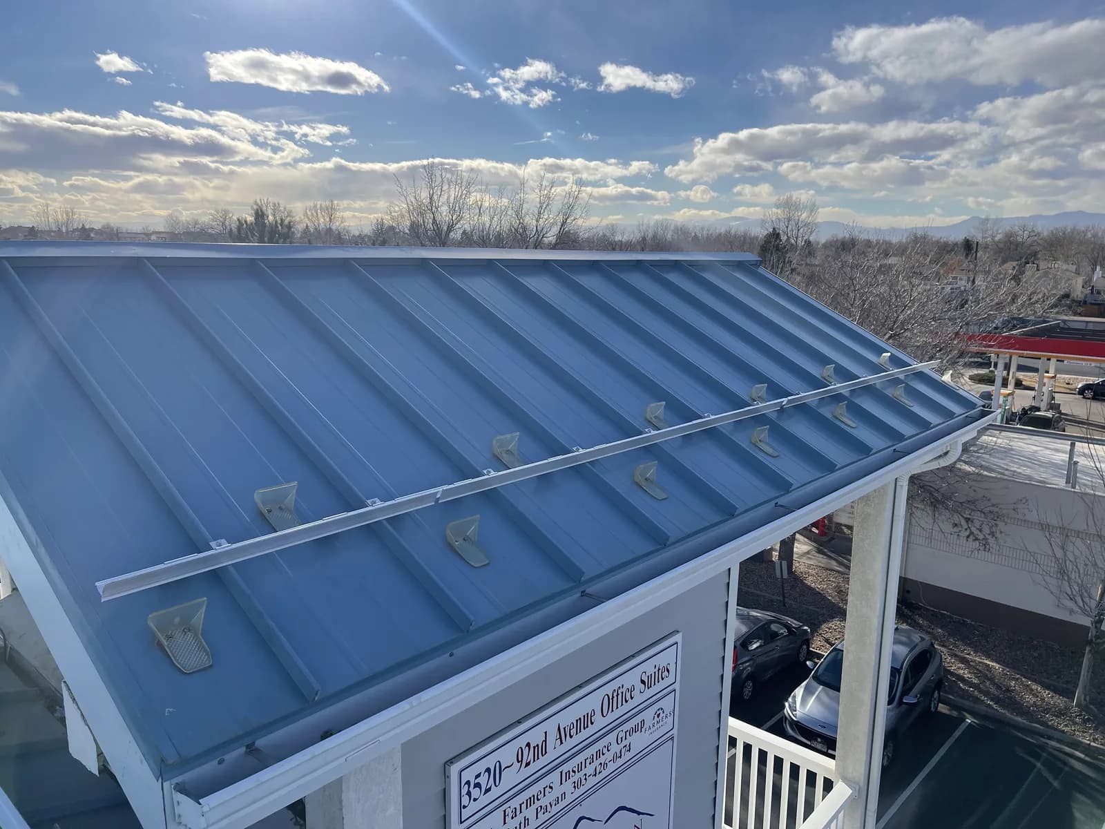 Blue-gray metal roof with snow-retention rails, trees and a cloudy sky beyond