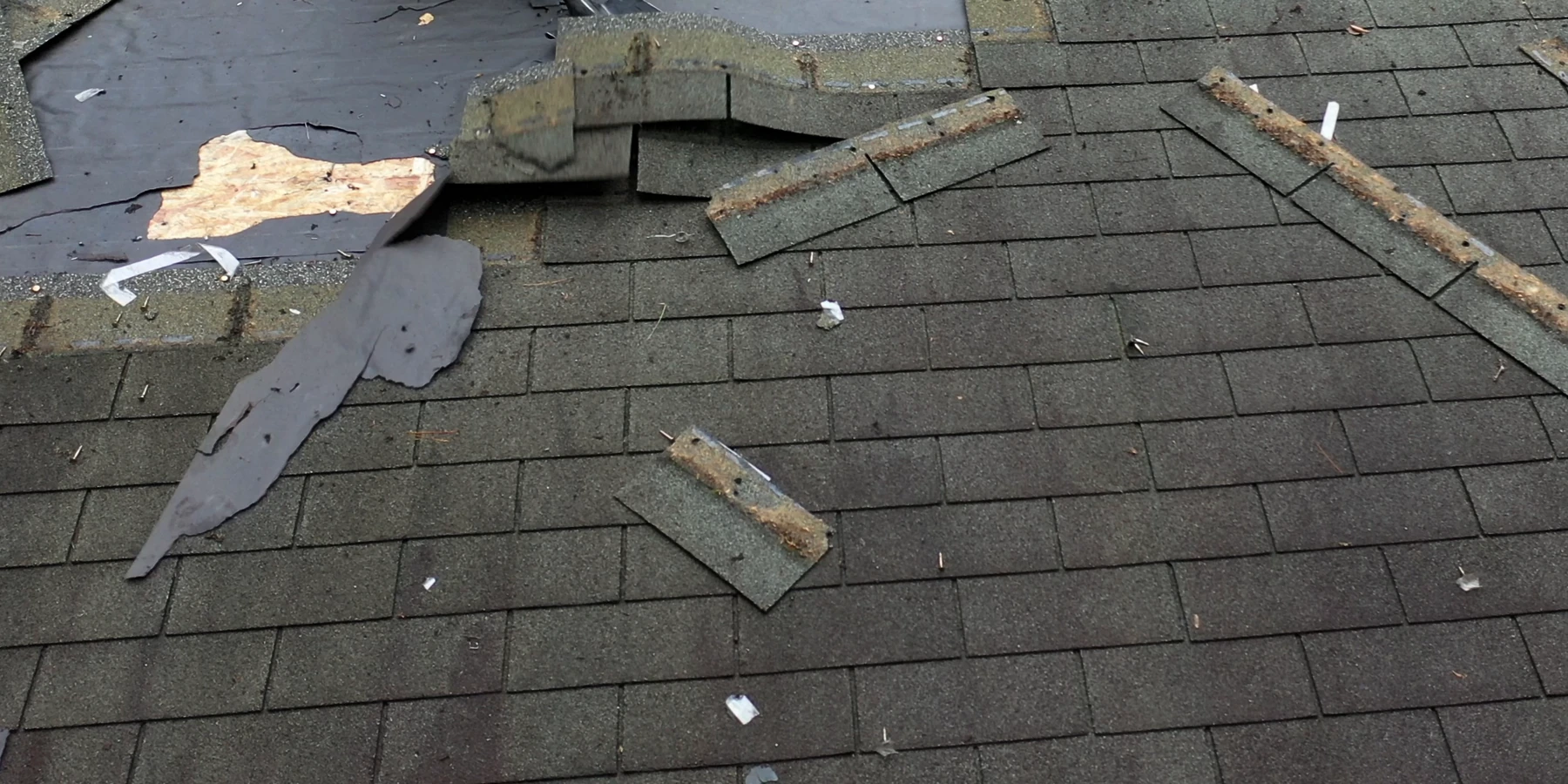 Roof tear-off showing remaining shingles, a dark sheet layer and an exposed patch of wood decking.